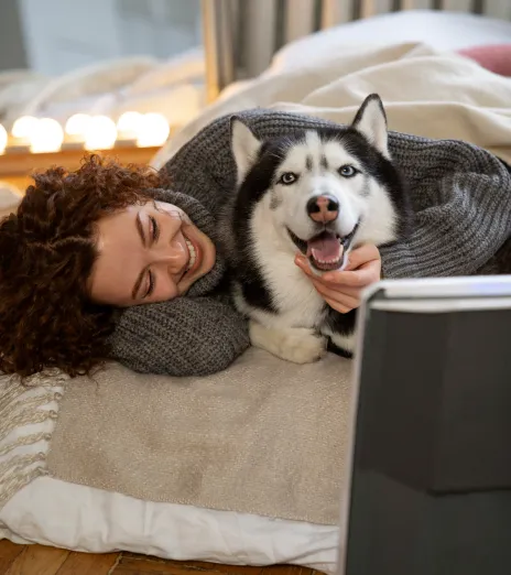 A woman smiling and cuddling her husky in a cozy, blanket-piled bed at home